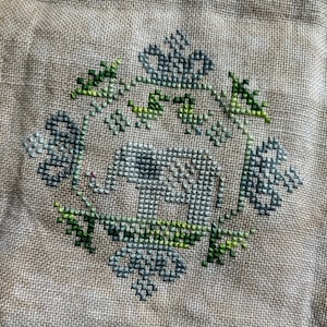 May include: A cross-stitch embroidery design featuring a gray elephant surrounded by green foliage and flowers.