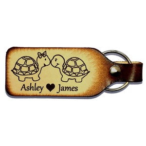 May include: A brown leather keychain with a key ring. The keychain has two turtles kissing with a heart and the names "Ashley" and "James" engraved on it.