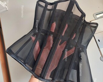 Peut inclure: Un corset noir fabriqué en tissu maille transparent avec des canaux de baleines verticaux. Le vêtement présente une silhouette structurée avec une encolure et un ourlet incurvés, et le mot Rememo est imprimé sur la maille.
