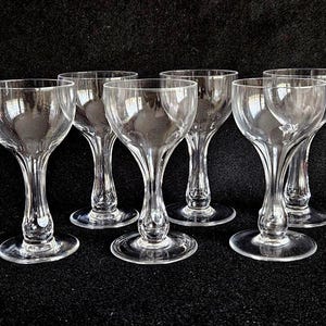 Peut inclure: Six verres à pied transparents avec des bols arrondis et des tiges délicates sont disposés sur une surface noire. Les verres ont un design classique, adapté pour servir diverses boissons. Les tiges ont une forme de bulbe décorative.
