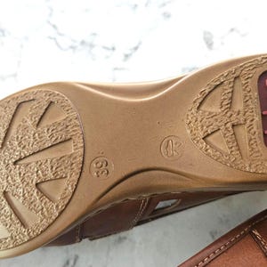 May include: Brown leather sandal with a textured sole. The sole features a geometric pattern and the brand name "riecker" in a red oval. The shoe size is 39.