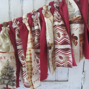 May include: A fabric garland with red and cream fabric strips tied together with knots. The fabric has a variety of patterns including plaid, floral, and geometric designs. The garland is perfect for adding a touch of rustic charm to any home.
