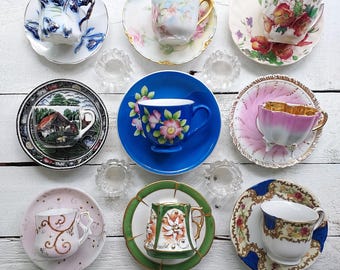 May include: A collection of ten vintage teacups and saucers with various floral and patterned designs. The teacups and saucers are arranged in a circle on a white wooden surface.