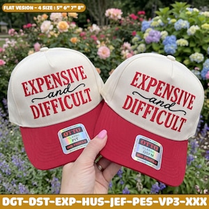 May include: Two cream-colored baseball caps with red brims, each featuring the embroidered red text "EXPENSIVE and DIFFICULT" on the front. Each cap includes a square holographic sticker on the brim with the text "OTTO CLASSIC".