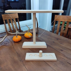 May include: Wooden ring toss game with a wooden base and a wooden platform with four holes. The game is set up on a wooden table.