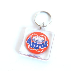 May include: A clear plastic keychain with a red and blue Astros logo. The logo features a baseball stadium with the word "Astros" in blue letters.