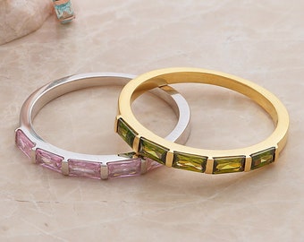 Pode incluir: Três anéis empilháveis com pedras preciosas coloridas. O anel superior é de ouro com pedras preciosas verdes, o anel do meio é de prata com pedras preciosas rosa e o anel inferior é de ouro rosa com pedras preciosas azuis.