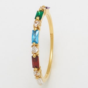 May include: A gold ring with a row of colorful gemstones. The ring features a red, blue, green, and white gemstone.