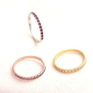 Könnte beinhalten: Drei zarte Ewigkeitsringe mit einer Reihe von Edelsteinen. Der Ring links hat lila Edelsteine, der mittlere Ring hat weiße Edelsteine und der Ring rechts hat rote Edelsteine.