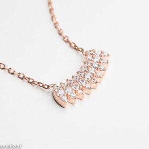May include: A rose gold necklace with a delicate chain and a sparkling, graduated, crystal pendant.