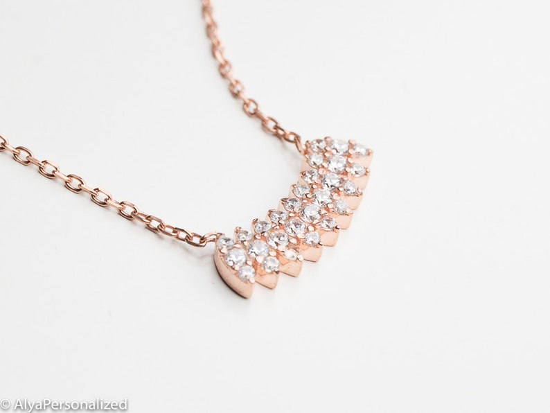 May include: A rose gold necklace with a delicate chain and a sparkling, graduated, crystal pendant.