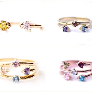 May include: Four gold rings with different colored gemstones. The rings are stacked on top of each other, with the top ring having a single gemstone and the bottom ring having three gemstones.