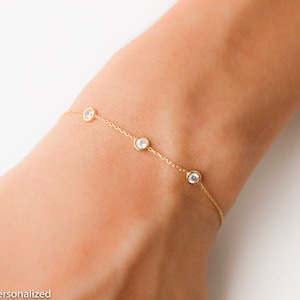 Puede incluir: Un delicado brazalete de cadena dorada con cuatro peque&ntilde;as piedras redondas transparentes.