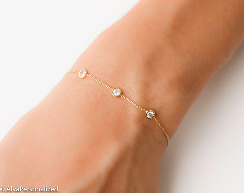 Puede incluir: Un delicado brazalete de cadena dorada con cuatro peque&ntilde;as piedras redondas transparentes.