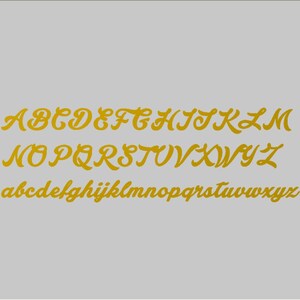 K&ouml;nnte beinhalten: Eine goldene Alphabetschrift mit Gro&szlig;- und Kleinbuchstaben. Die Buchstaben sind im Kursivschrift-Stil gestaltet.