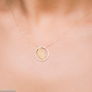 May include: A gold necklace with a delicate chain and a pendant featuring a fingerprint design surrounded by small clear stones.