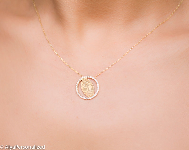 May include: A gold necklace with a delicate chain and a pendant featuring a fingerprint design surrounded by small clear stones.