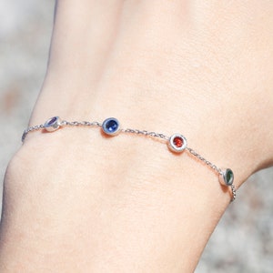Puede incluir: Un brazalete de cadena de plata con cuatro peque&ntilde;as piedras redondas. Las piedras preciosas son azules, rojas, verdes y moradas.