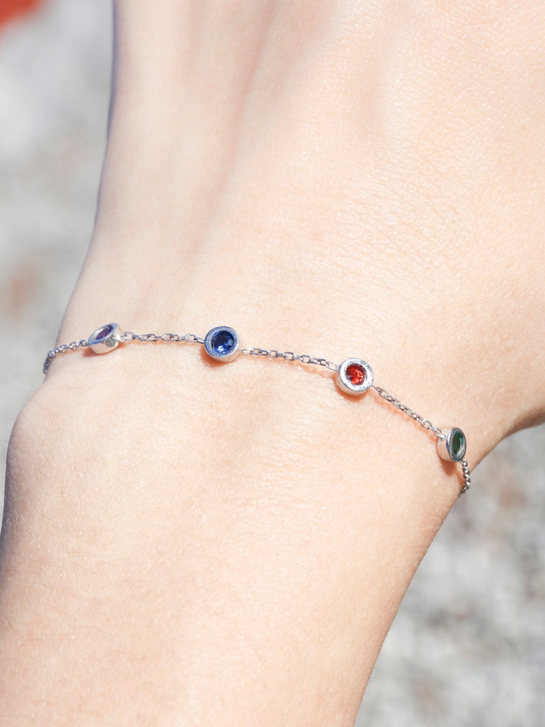 Puede incluir: Un brazalete de cadena de plata con cuatro peque&ntilde;as piedras redondas. Las piedras preciosas son azules, rojas, verdes y moradas.