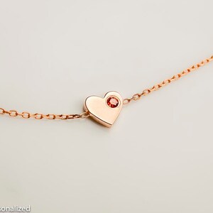 May include: A rose gold necklace with a heart pendant featuring a small red gemstone in the center.