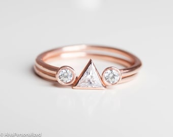 May include: A rose gold ring set with a triangular shaped diamond and two round diamonds.