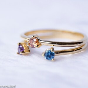 May include: A gold ring with four small gemstones. The gemstones are purple, orange, blue, and a lighter shade of orange.