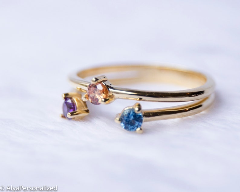 May include: A gold ring with four small gemstones. The gemstones are purple, orange, blue, and a lighter shade of orange.