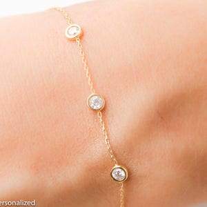 Puede incluir: Un delicado brazalete de cadena dorada con cuatro peque&ntilde;as piedras redondas transparentes.