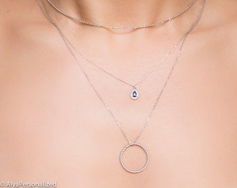 Puede incluir: Un collar de plata con tres cadenas. La cadena superior tiene un diseño delicado y con cuentas. La cadena del medio tiene un colgante en forma de lágrima con una piedra preciosa azul rodeada de piedras preciosas transparentes más pequeñas. La cadena inferior tiene un colgante circular.
