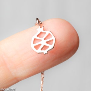 May include: A silver necklace with a delicate pomegranate pendant. The pendant is a cutout design, showing the inside of the fruit.