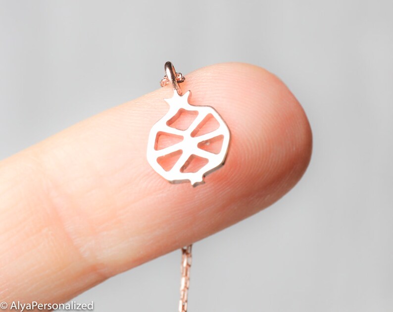 May include: A silver necklace with a delicate pomegranate pendant. The pendant is a cutout design, showing the inside of the fruit.