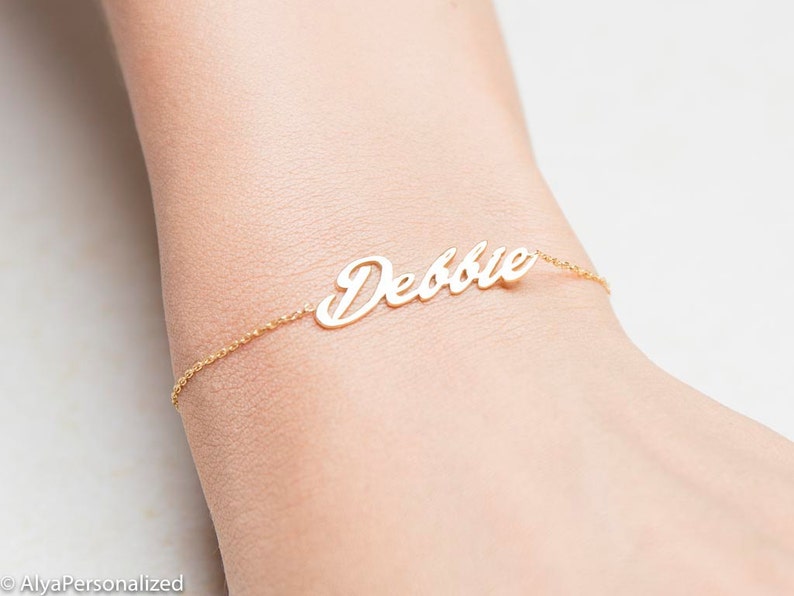 K&ouml;nnte beinhalten: Ein goldenes Kettenarmband mit dem Namen "Debbie" in Kursivschrift.