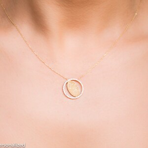 May include: A gold necklace with a delicate chain and a round pendant featuring a fingerprint design. The pendant is surrounded by a circle of small diamonds.