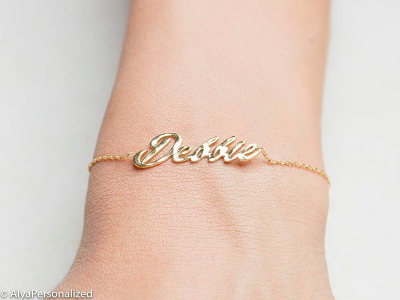 K&ouml;nnte beinhalten: Ein goldenes Kettenarmband mit dem Namen "Debbie" in Kursivschrift.