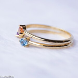 May include: A gold ring with three small gemstones. The gemstones are blue, orange, and purple.