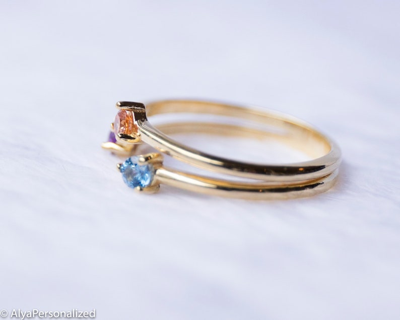 May include: A gold ring with three small gemstones. The gemstones are blue, orange, and purple.