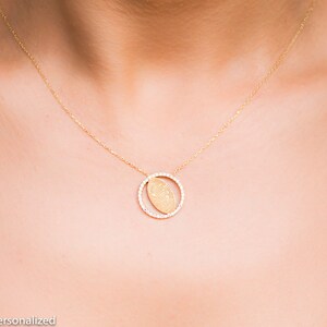 May include: A gold necklace with a delicate chain and a pendant featuring a fingerprint design inside a circle of small diamonds.