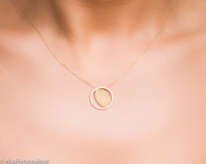 May include: A gold necklace with a delicate chain and a pendant featuring a fingerprint design inside a circle of small diamonds.