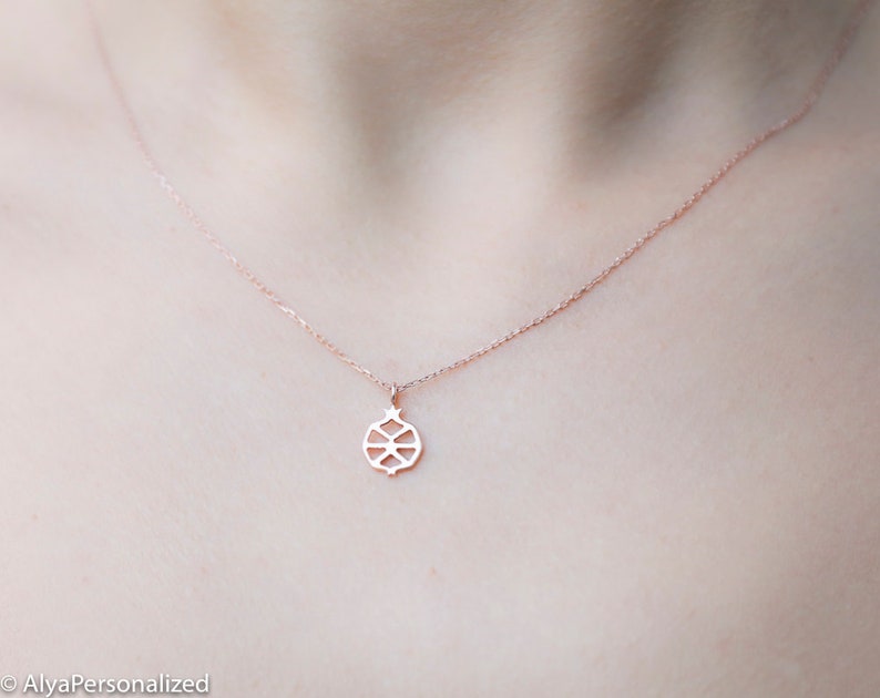 May include: A delicate rose gold necklace with a geometric pendant in the shape of a pomegranate. The pendant is made of a thin metal and has a detailed design.