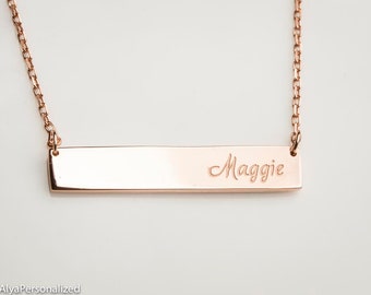 Könnte beinhalten: Halskette aus Roségold mit einem gravierten Balken mit dem Namen "Maggie" in Schreibschrift. Die Halskette hat eine zarte Kette und ein poliertes Finish, ideal für personalisierten Schmuck.