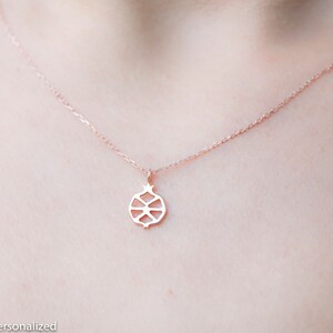 May include: A delicate rose gold necklace with a simple, geometric pomegranate pendant.