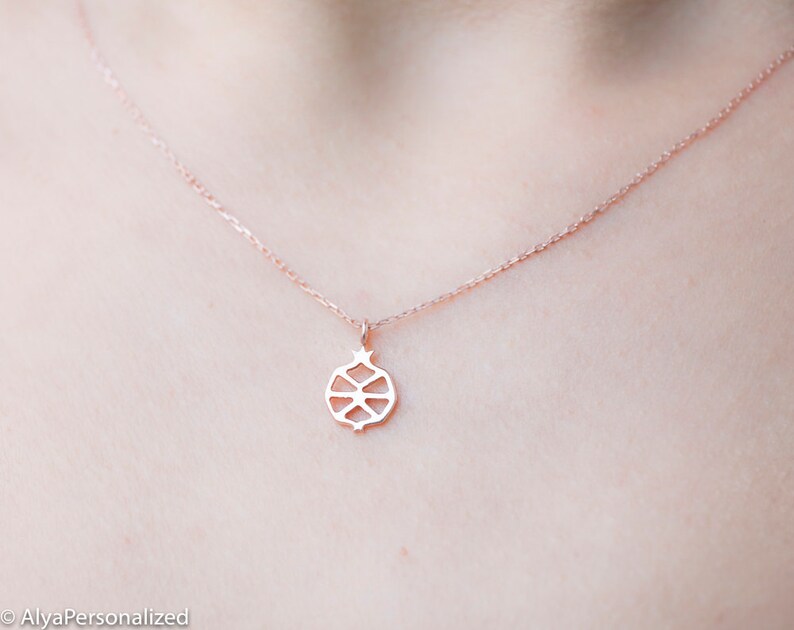 May include: A delicate rose gold necklace with a simple, geometric pomegranate pendant.