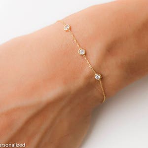 Puede incluir: Un delicado brazalete de cadena dorada con cuatro peque&ntilde;as piedras redondas transparentes.