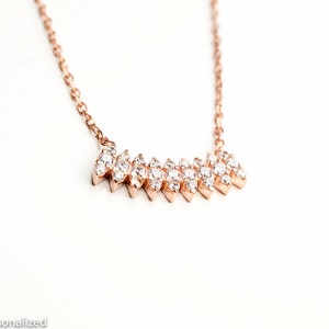 May include: A rose gold necklace with a delicate chain and a sparkling diamond-like pendant in the shape of a chevron.