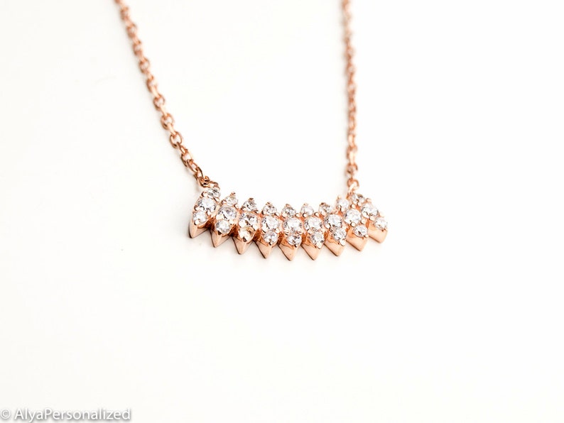 May include: A rose gold necklace with a delicate chain and a sparkling diamond-like pendant in the shape of a chevron.