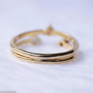 May include: A gold ring with two bands and three small gemstones. The ring is on a white background.