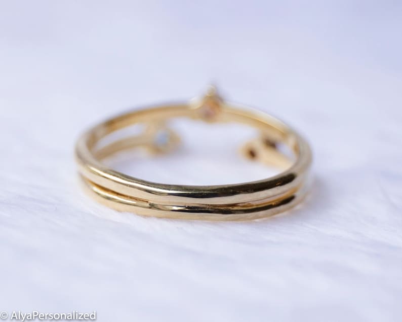 May include: A gold ring with two bands and three small gemstones. The ring is on a white background.
