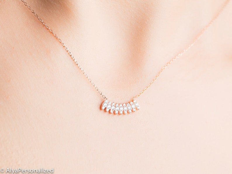 May include: A delicate rose gold necklace with a small, curved row of sparkling clear cubic zirconia stones.