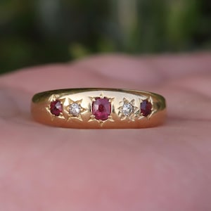 May include: A gold ring with five gemstones. The ring features three oval-cut rubies and two smaller diamonds set in starburst settings. The ring is a classic design, likely vintage or antique.