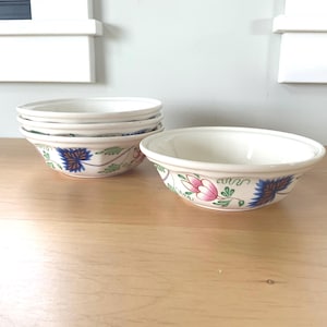 May include: Set of four white ceramic bowls with a floral design in shades of blue, green, pink, and yellow. The bowls are stacked on top of each other.